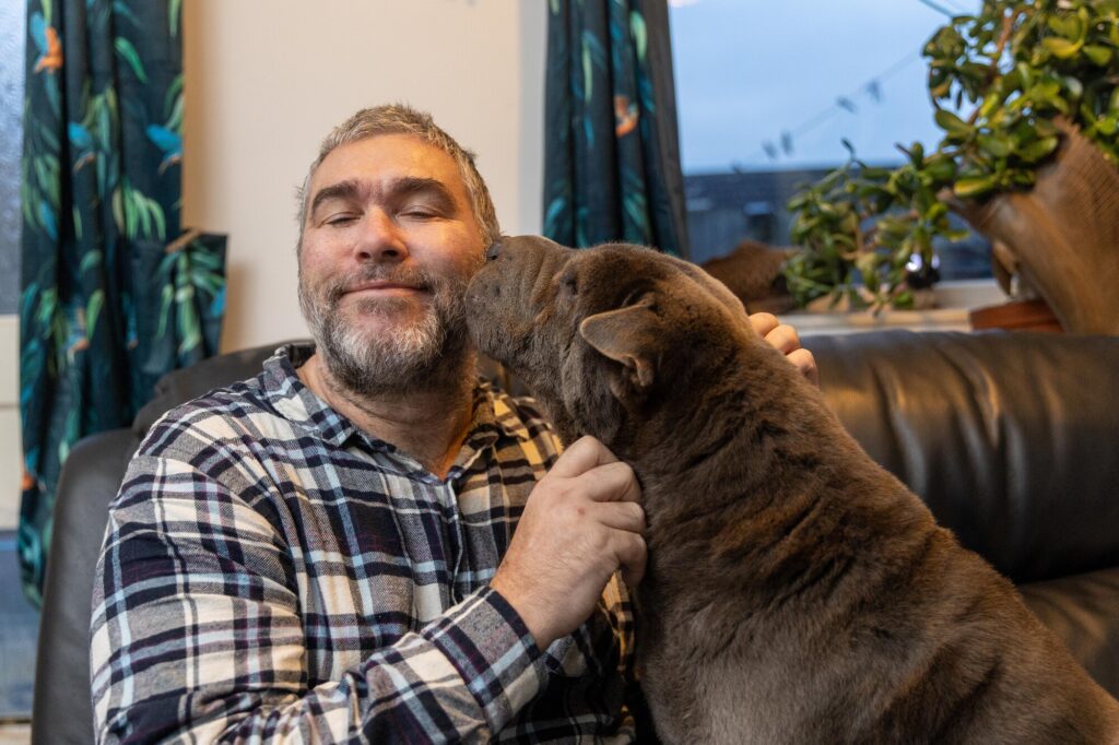 John Goude intervened as a dog attacked a teenager with many bystanders agreeing that John saved the teenager’s life. The dog had already attacked the mother of the teenager. March Monday 04 November 2024. Pictured relaxing at home with his own dog, Lilly by Terry Harris