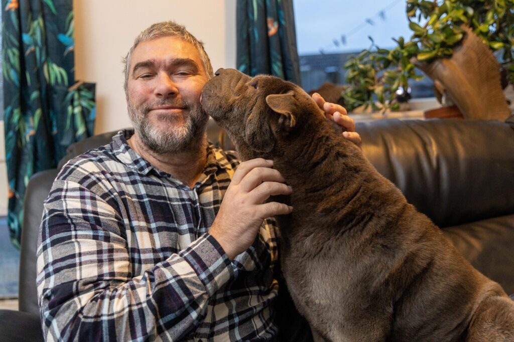 John Goude intervened as a dog attacked a teenager with many bystanders agreeing that John saved the teenager’s life. The dog had already attacked the mother of the teenager. March Monday 04 November 2024. Pictured relaxing at home with his own dog, Lilly by Terry Harris